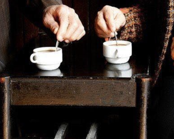 Two pairs of hands stirring coffee cups on a wooden bench